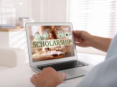 Male sitting at a table with a laptop open, looking at schloarships.